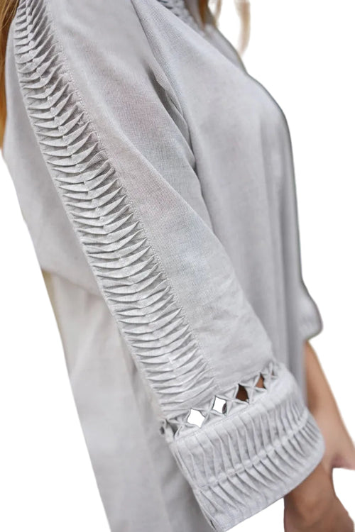 Close-up of a light gray garment with intricate detailing on the sleeve