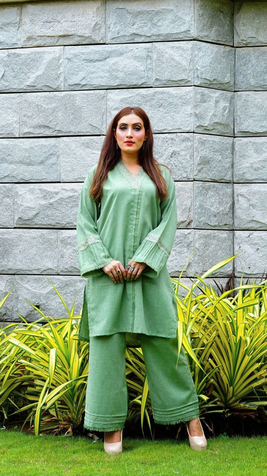 Woman in a green outfit standing against a stone wall with plants.
