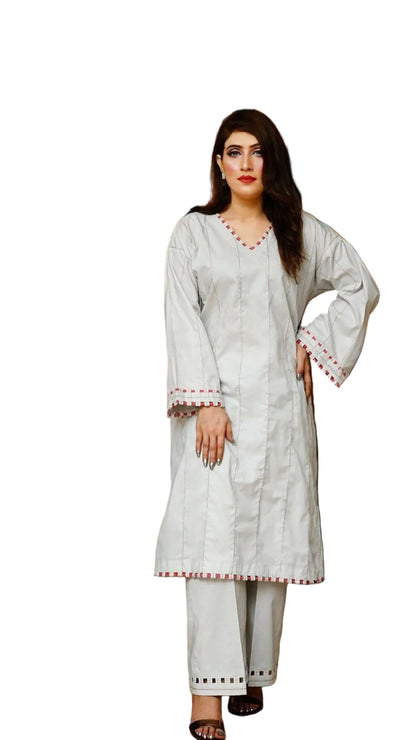 Woman in a white traditional outfit standing in a room with wooden walls and a lamp.