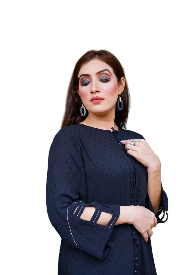 Woman in a black outfit with cut-out sleeves sitting on a stone surface with greenery in the background.