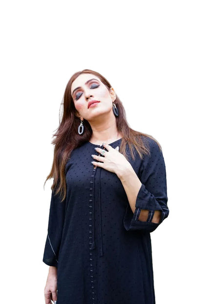 Woman wearing a  black coat standing outdoors with plants in the background