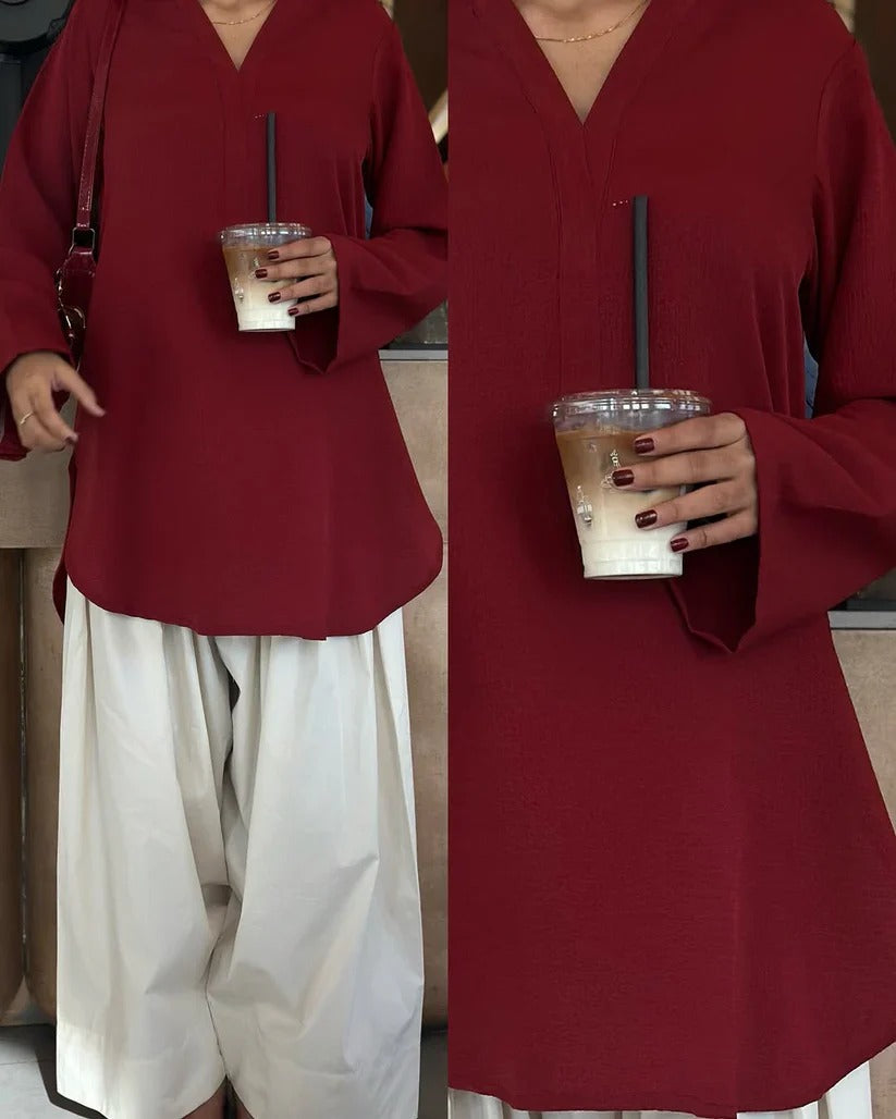 New Arrival from Shadow Shenaz: Beautiful young woman wearing a rich maroon V-neck loose kurti with wide sleeves paired with off-white wide leg palazzo pants. She is standing elegantly holding a matching maroon handbag in a luxurious indoor setting.