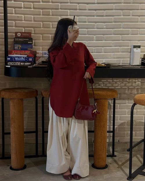 New Arrival from Shadow Shenaz: Beautiful young woman wearing a rich maroon V-neck loose kurti with wide sleeves paired with off-white wide leg palazzo pants. She is standing elegantly holding a matching maroon handbag in a luxurious indoor setting.